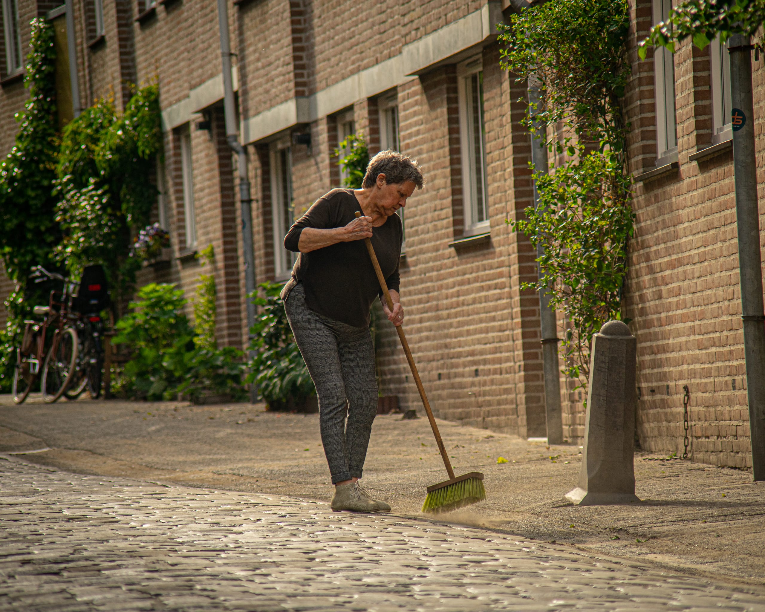 Street photograph: a woman sweeping a cobbled street
